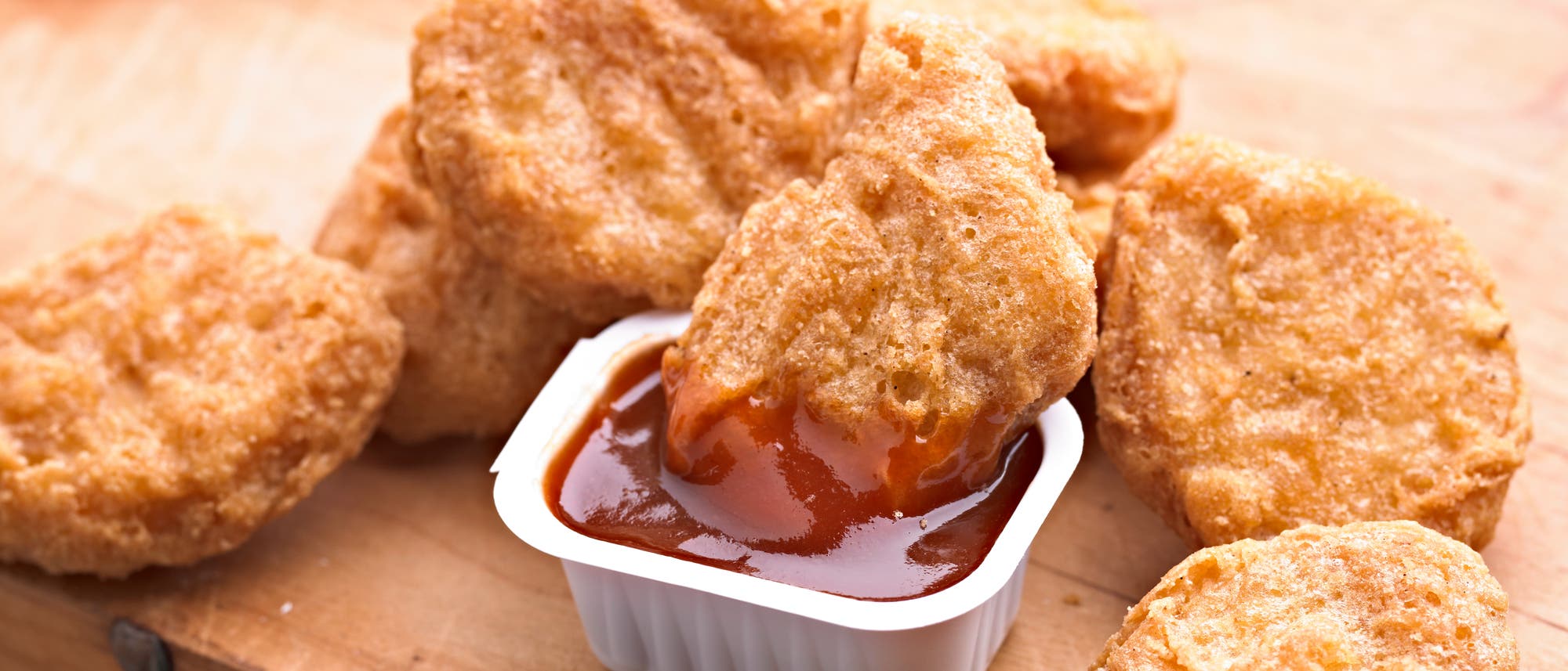 Mehrere panierte Chicken Nuggets. Einer davon liegt in einer kleinen Plastikschale mit einer rötlichen Soße. Mehrere panierte Chicken Nuggets. Einer davon liegt in einer kleinen Plastikschale mit einer rötlichen Soße.