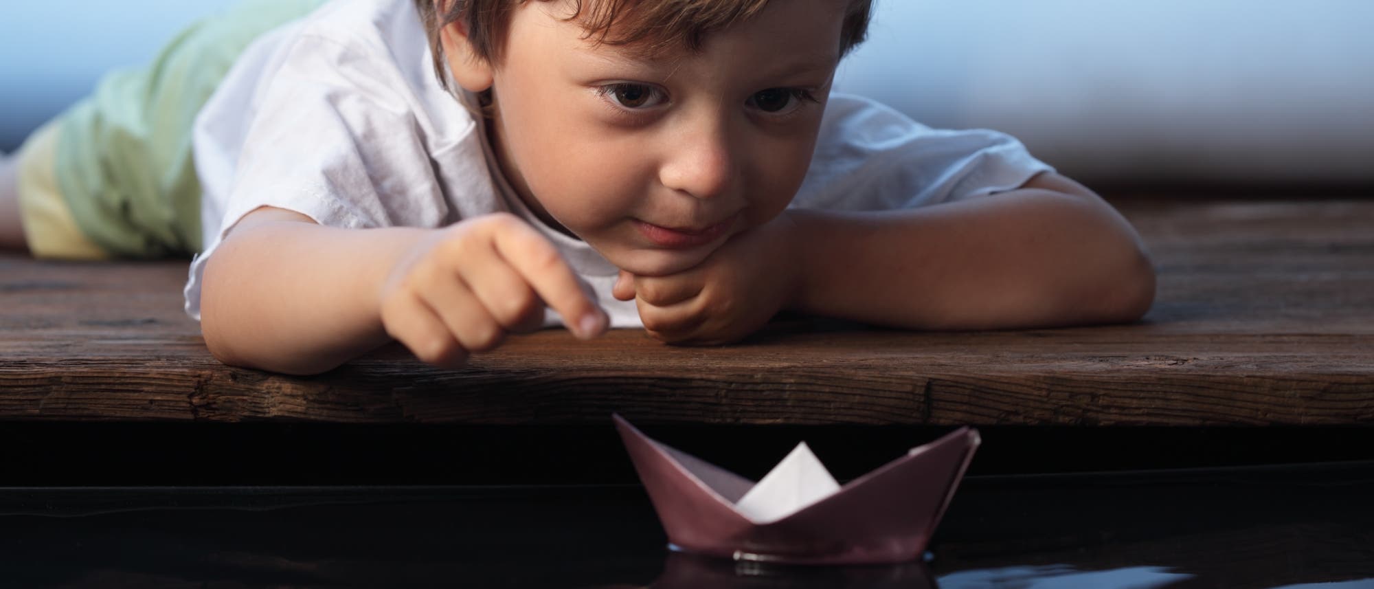 Ein kleiner Junge spielt mit einem Papierboot im Wasser Ein kleiner Junge spielt mit einem Papierboot im Wasser
