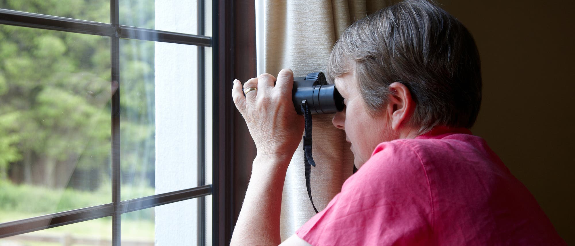 Frau schaut mit dem Fernglas aus dem Fenster Frau schaut mit dem Fernglas aus dem Fenster