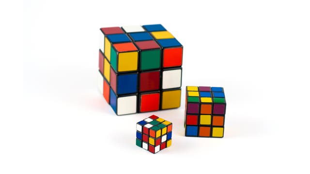 Drei Rubik-Würfel unterschiedlicher Größe auf weißem Grund.