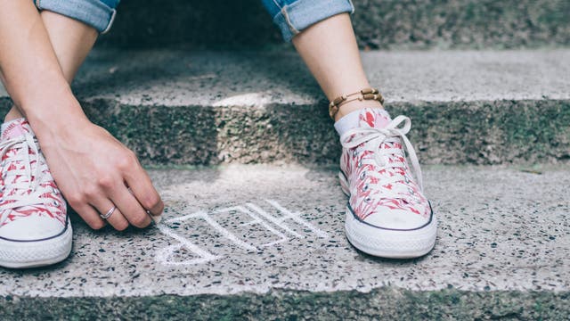 Jugendliche schreibt "HELP" auf die Treppe zwischen ihren Füßen