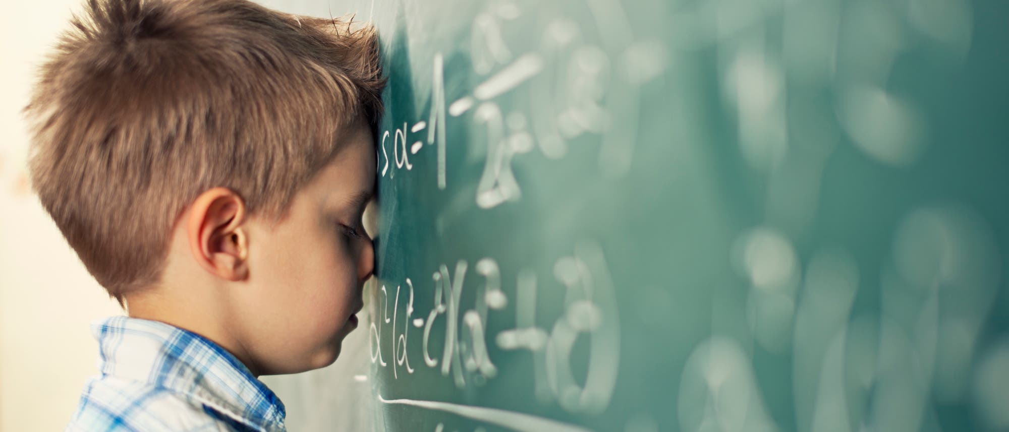 Ein Schüler lehnt mit dem Kopf an einer Tafel mit Mathe-Formeln.