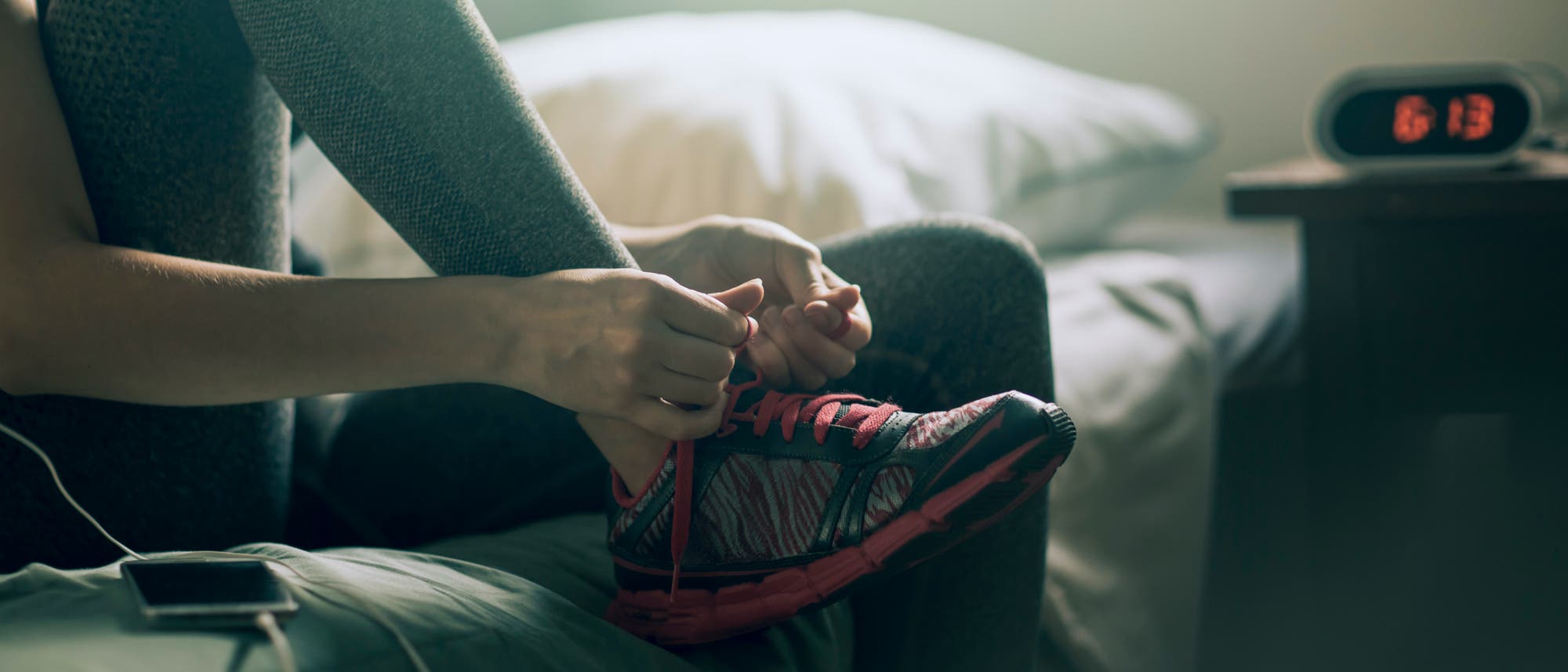 Frau zieht sich morgens am Bett ihre Sportschuhe an Frau zieht sich morgens am Bett ihre Sportschuhe an