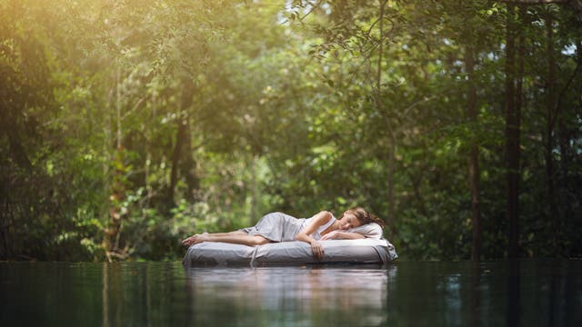 Traumsequenz: Frau liegt schlafend auf einem schwimmenden Bett in einem Wald