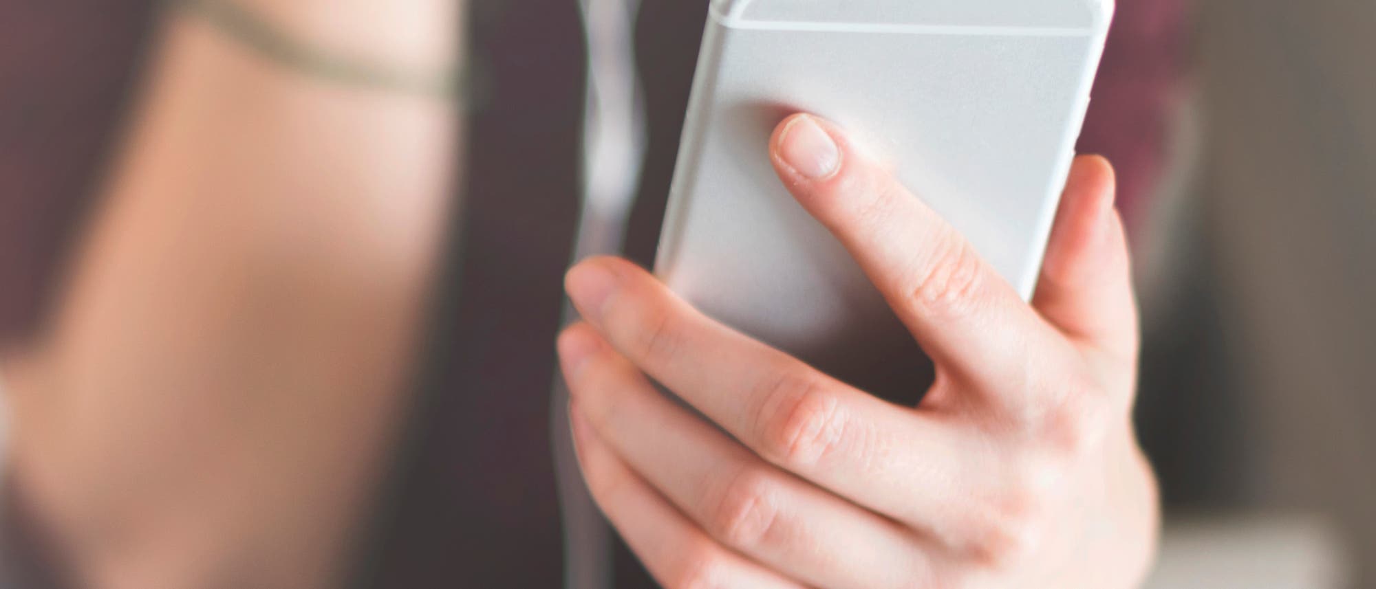 Eine junge Frau sieht in sitzender Position auf ihr Smartphone. Eine junge Frau sieht in sitzender Position auf ihr Smartphone.