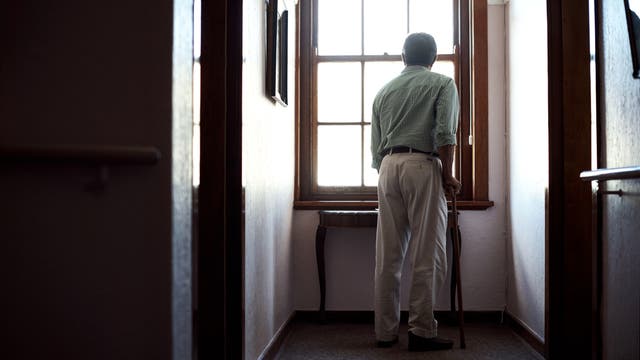 Ein älterer Mann mit Stock steht am Fenster.