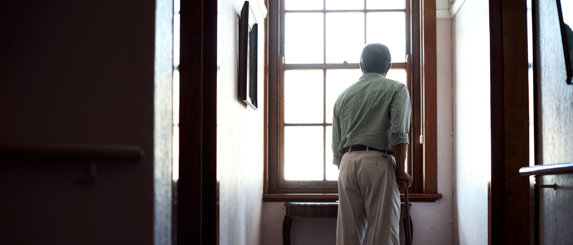 Ein älterer Mann mit Stock steht am Fenster.