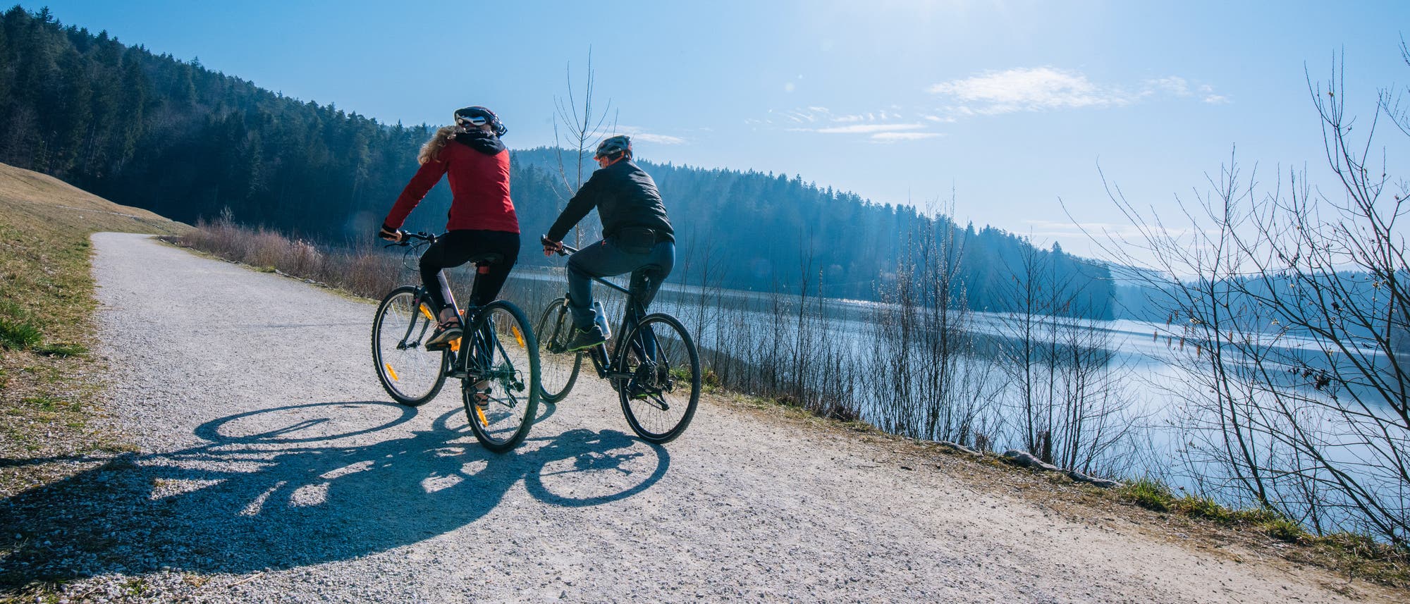 Zwei Personen fahren Fahrrad auf einer Straße am Seeufer. Zwei Personen fahren Fahrrad auf einer Straße am Seeufer.