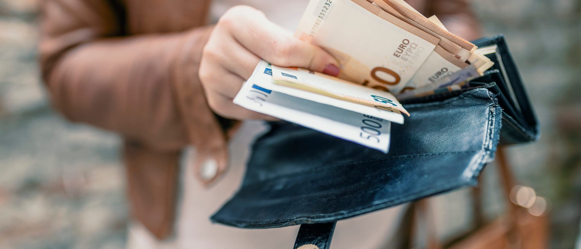 Eine Frau hält einen Geldbeutel mit Scheinen darin in der Hand Eine Frau hält einen Geldbeutel mit Scheinen darin in der Hand