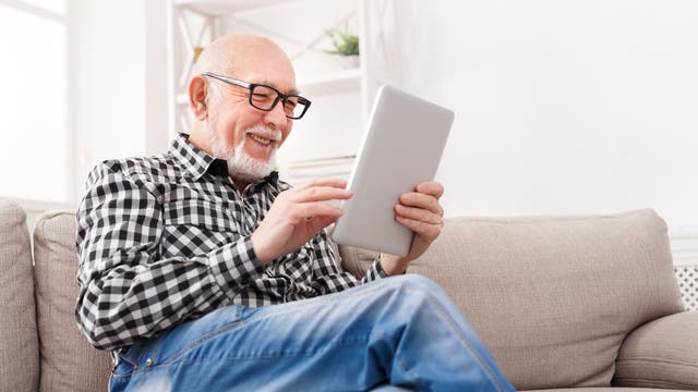 Älterer Mann guckt lächelnd auf sein Tablet.