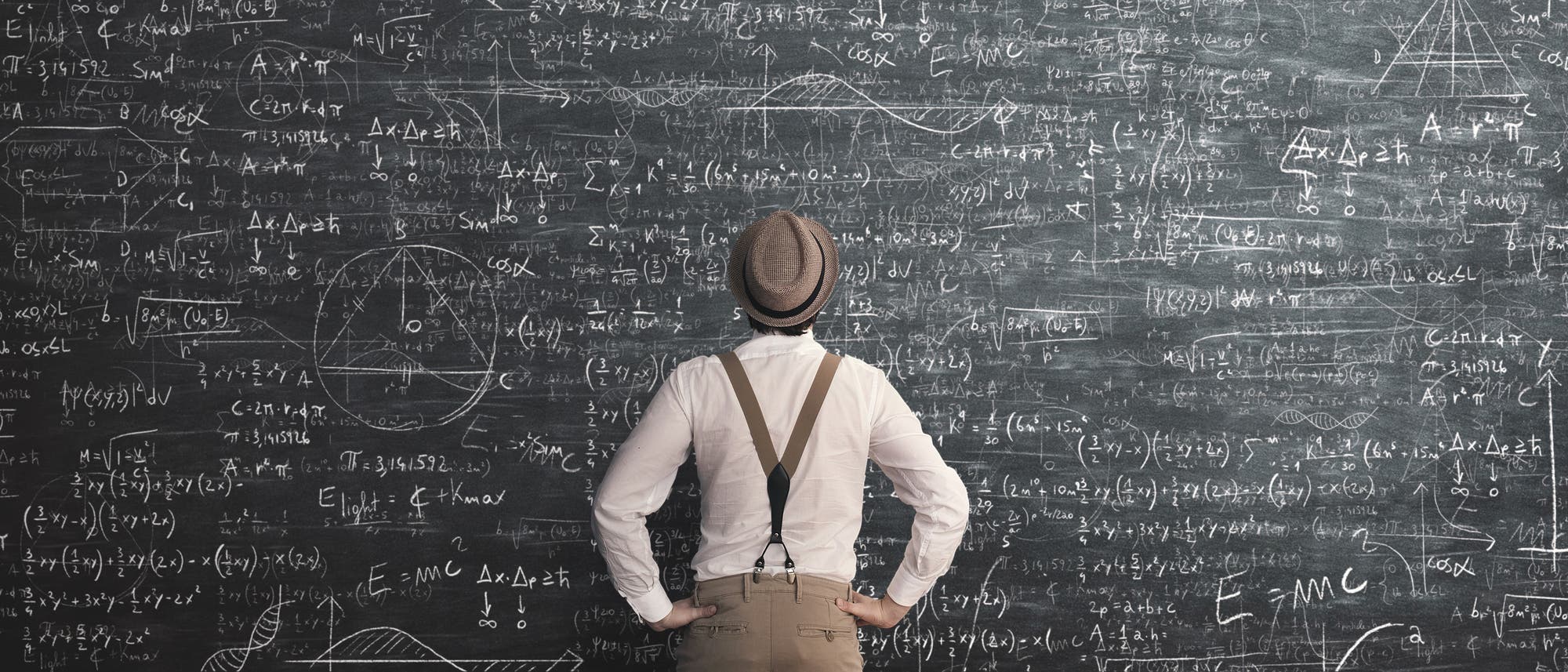 Ein Mann steht vor einer riesigen Tafel voller mathematischer Berechnungen Ein Mann steht vor einer riesigen Tafel voller mathematischer Berechnungen
