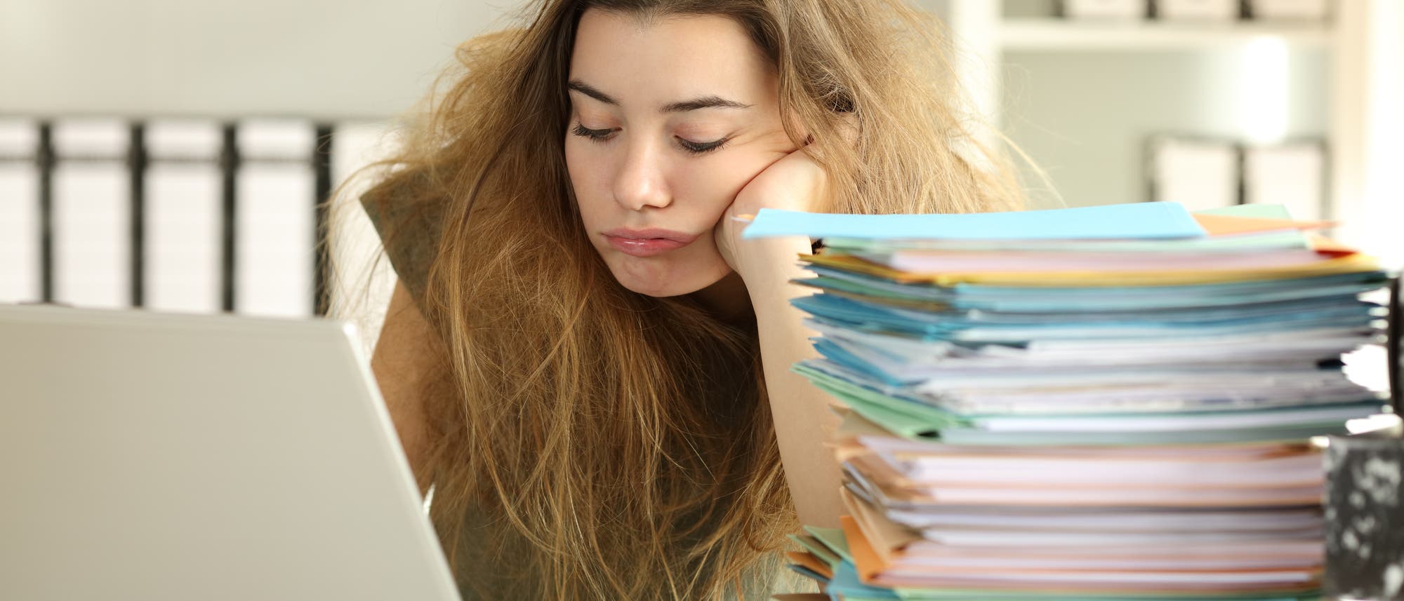 Muss ich? Könnte ich nicht etwas anderes machen und mich vor der Arbeit drücken? Vielleicht denkt das die Frau, die mit einer Menge Papierkram gelangweilt vor ihrem Laptop den Kopf in die Hand stützt. Muss ich? Könnte ich nicht etwas anderes machen und mich vor der Arbeit drücken? Vielleicht denkt das die Frau, die mit einer Menge Papierkram gelangweilt vor ihrem Laptop den Kopf in die Hand stützt.