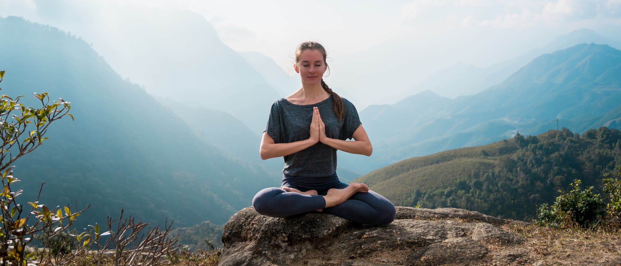 Junge Frau im Yogasitz vor Bergpanorama Junge Frau im Yogasitz vor Bergpanorama