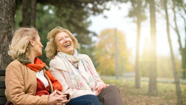 Zwei Frauen sitzen auf einer Parkbank und lachen