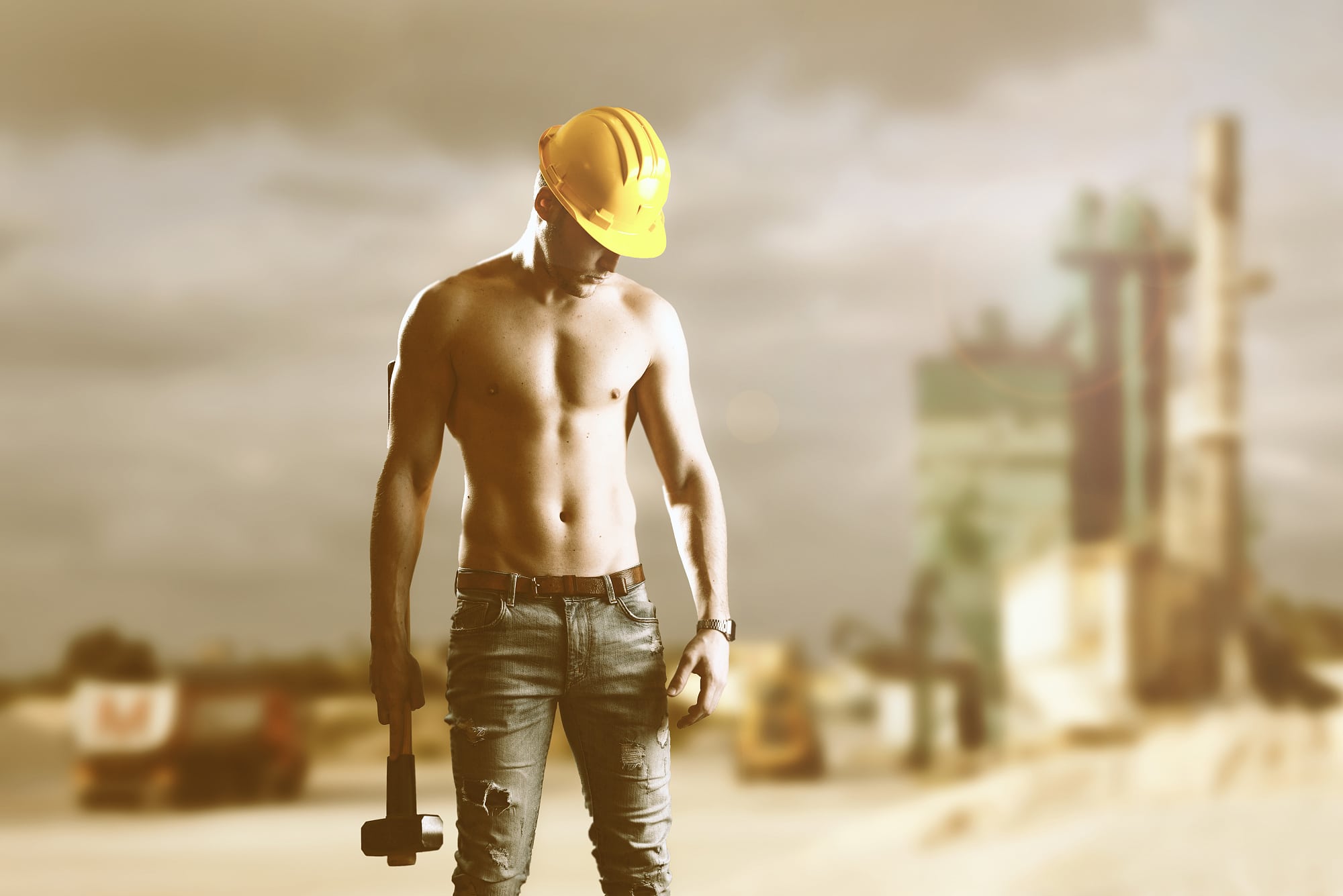 Junger Mann ohne T-Shirt, aber mit Helm und Hammer beobachtet angestrengt eine Stelle neben seinem linken Fuß Junger Mann ohne T-Shirt, aber mit Helm und Hammer beobachtet angestrengt eine Stelle neben seinem linken Fuß