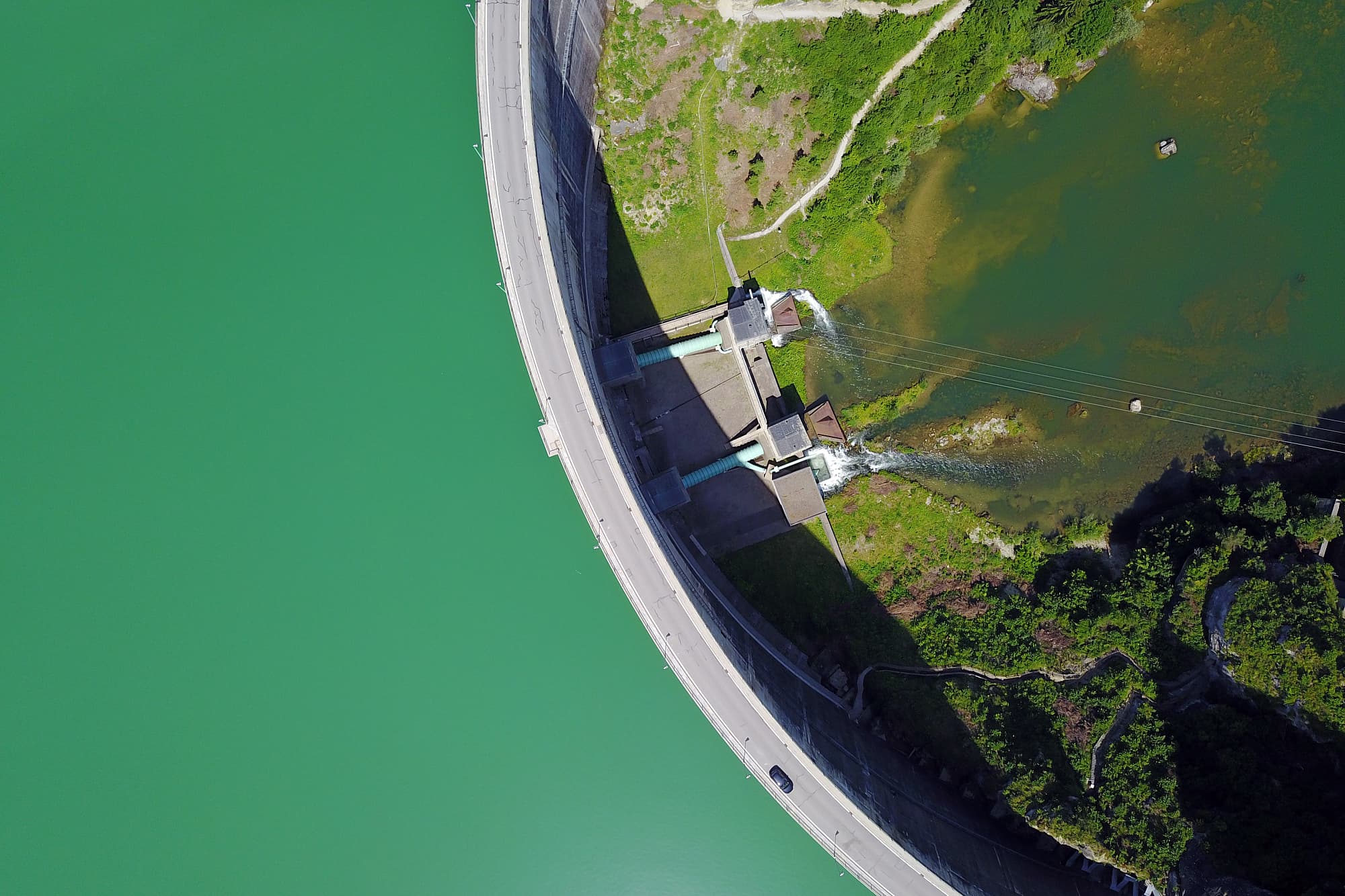 Blick direkt von oben auf die Staumauer eines großen Reservoirs. Links das türkise Wasser des Sees, rechts ein Tal. Blick direkt von oben auf die Staumauer eines großen Reservoirs. Links das türkise Wasser des Sees, rechts ein Tal.