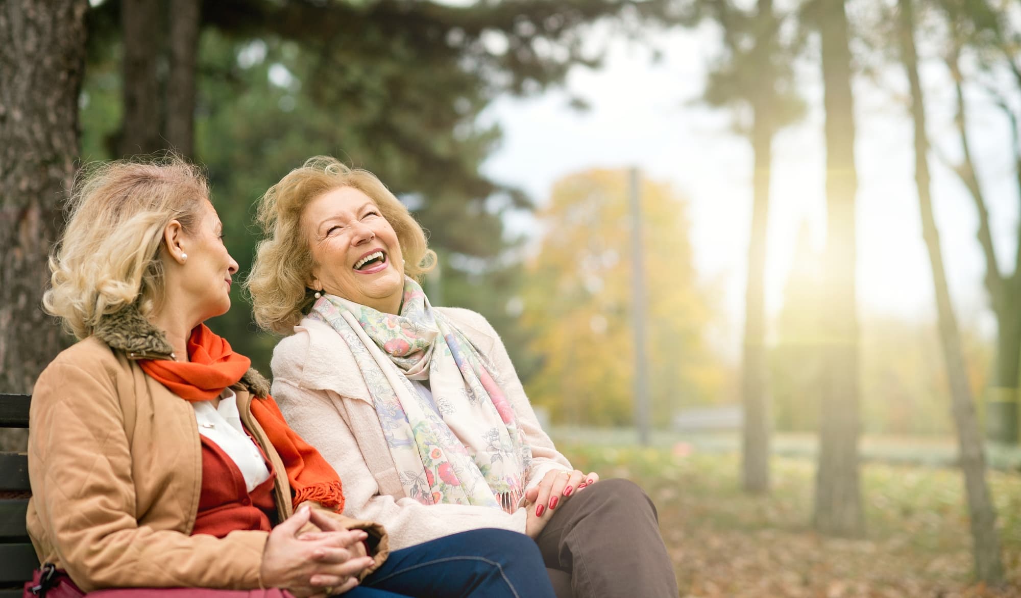 Zwei Frauen sitzen auf einer Parkbank und lachen Zwei Frauen sitzen auf einer Parkbank und lachen